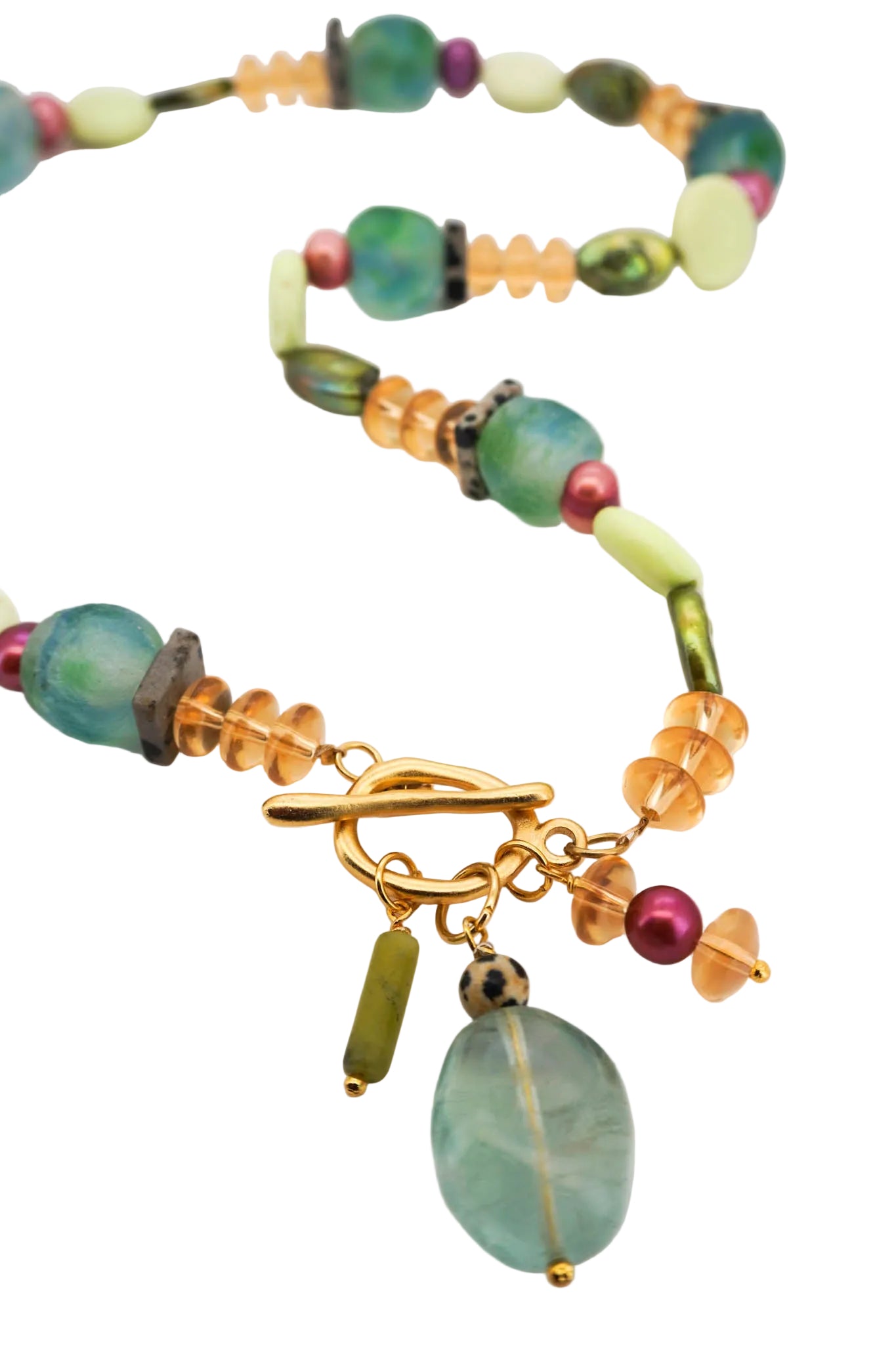 A beaded necklace with a gold toggle clasp, featuring translucent light green beads, textured green stone beads, amber-orange faceted beads, and a large hanging oval light green stone charm, displayed on a white background.